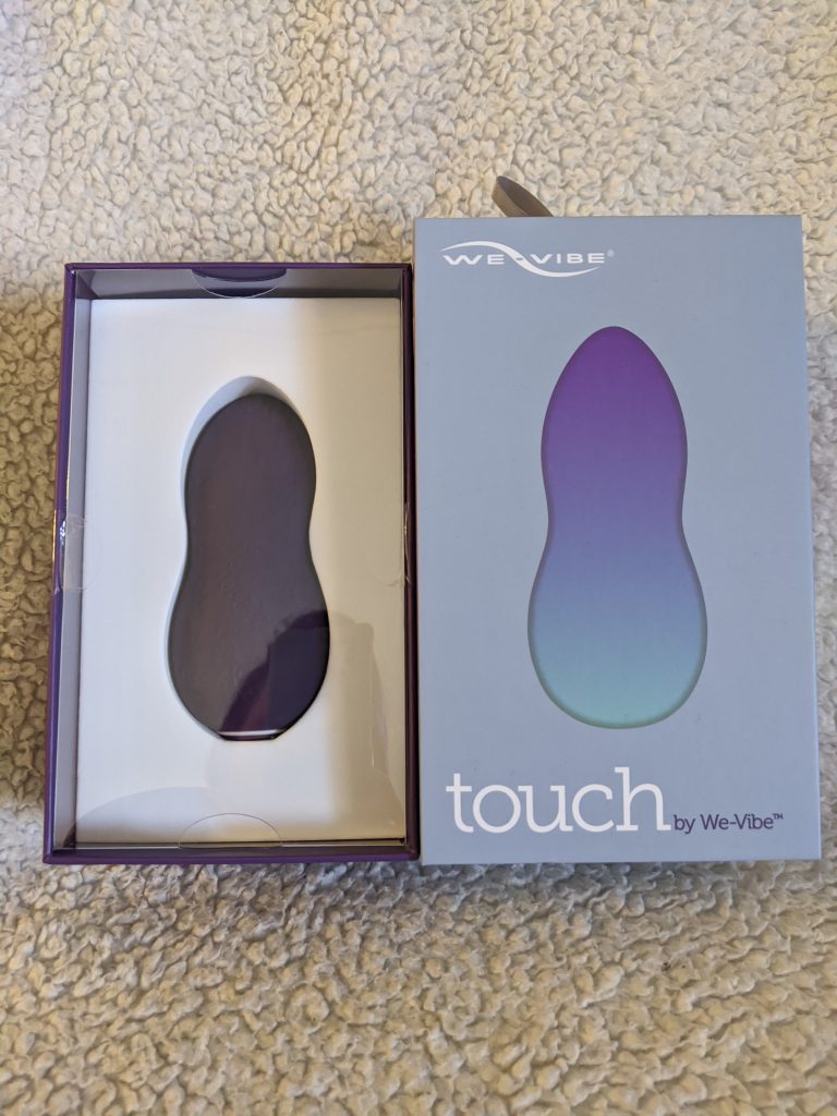 Image of the We-vibe box cover lifted off the we-vibe and the toy in its box with a reflection of me, the photographer, in the plastic. 