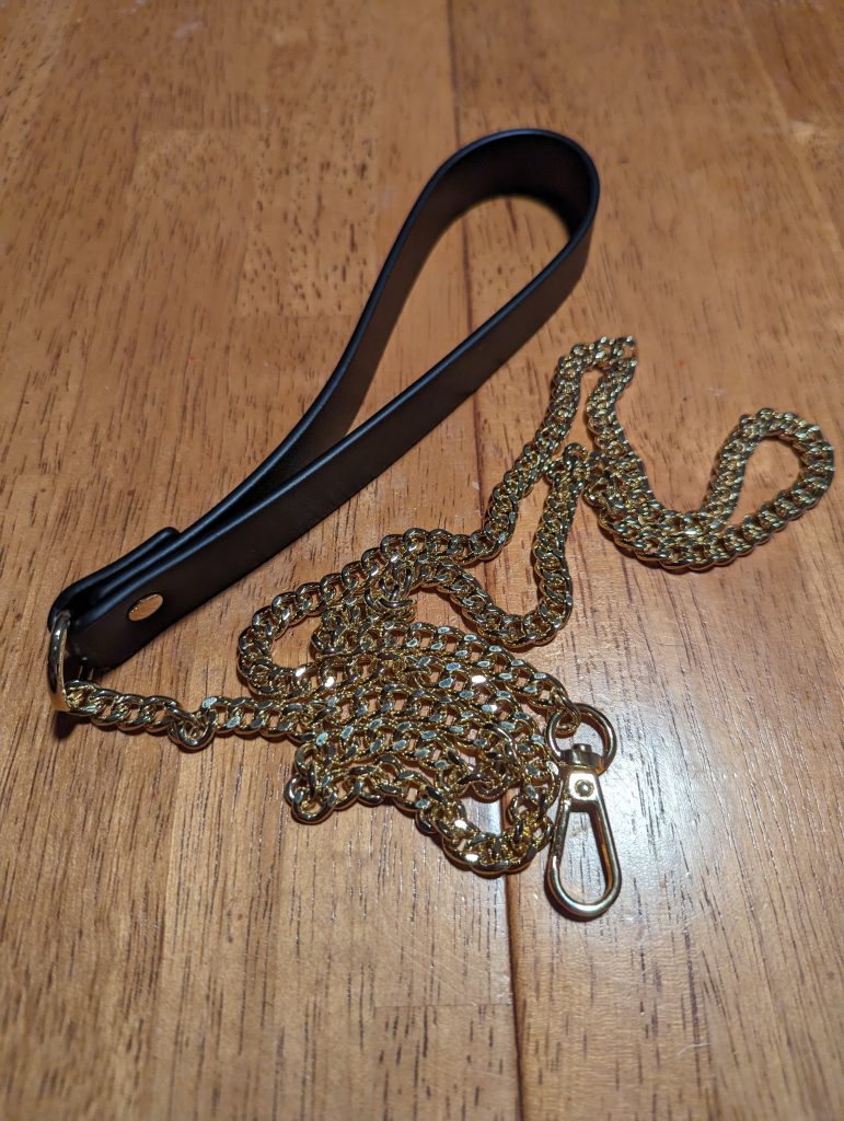 Leash on table. Black leather handle with gold chain