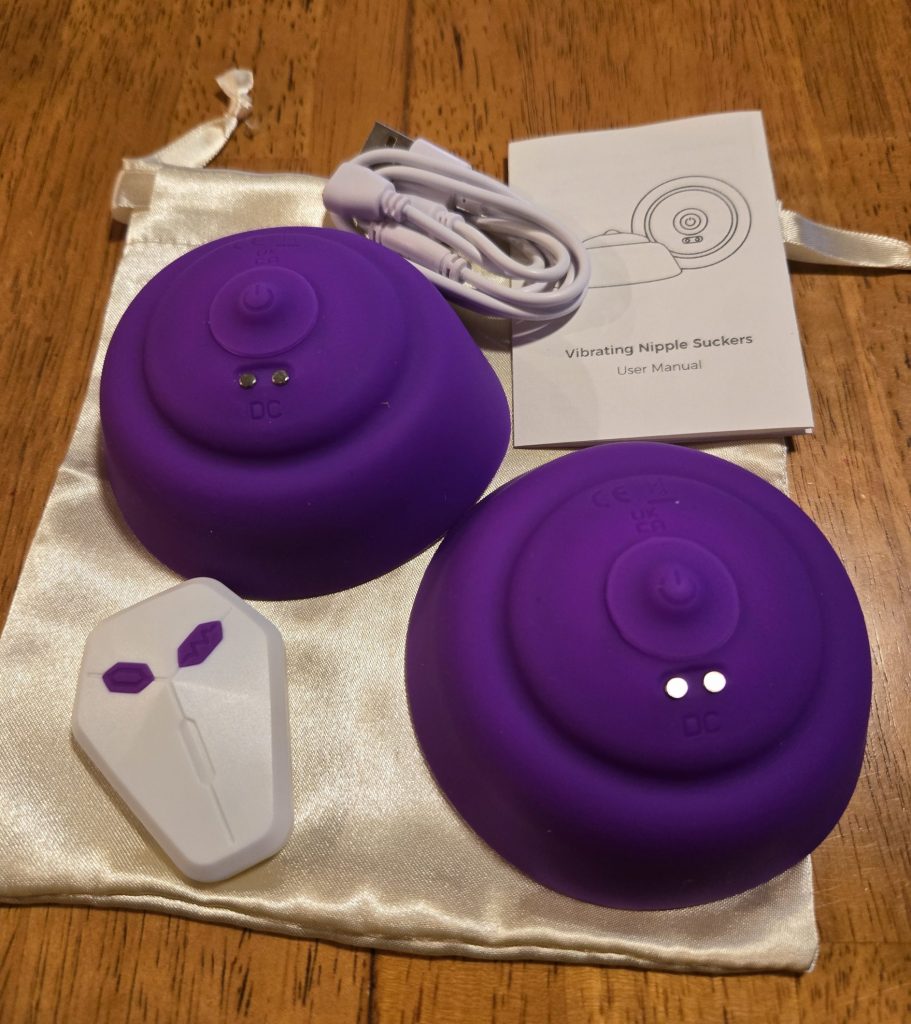 Two nipple suckers that are large purple discs, a remote control, charger, instructions, and satin bag